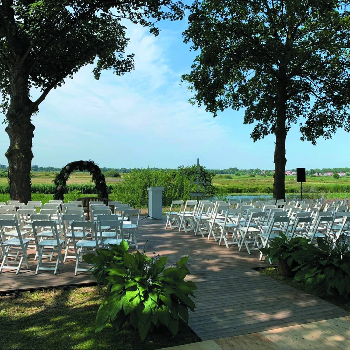 Bruiloftsceremonie buiten met witte stoelen en bloemenboog