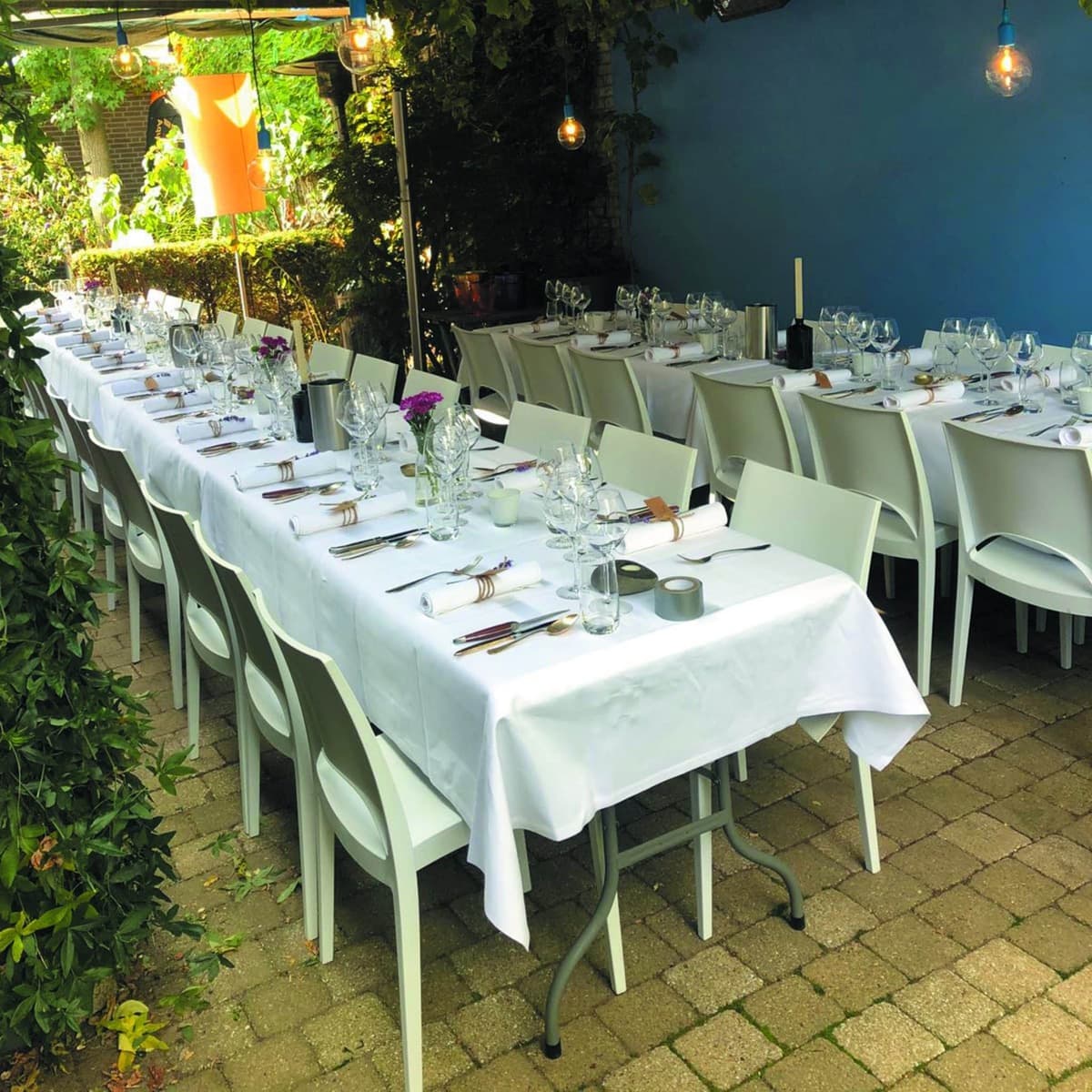 Lange diner tafel buiten met witte stoelen en lampionnen